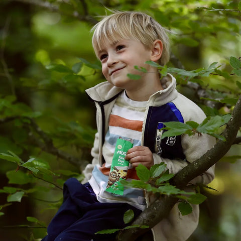 Junge sitzt auf einem Ast von einem Baum mit dem MOGLi Kakao Riegel in der Hand