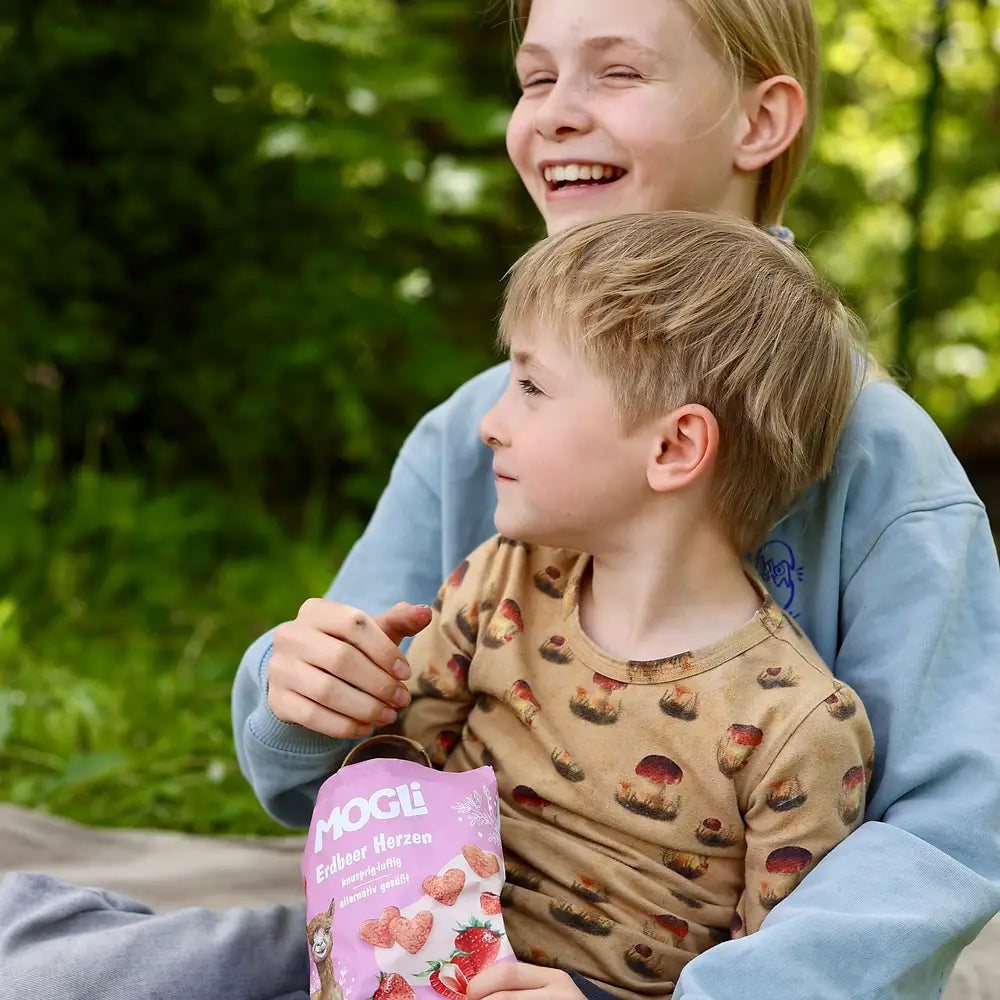 Snackmoment von Geschwistern mit den MOGLi Erdbeer Herzen im Wald. 