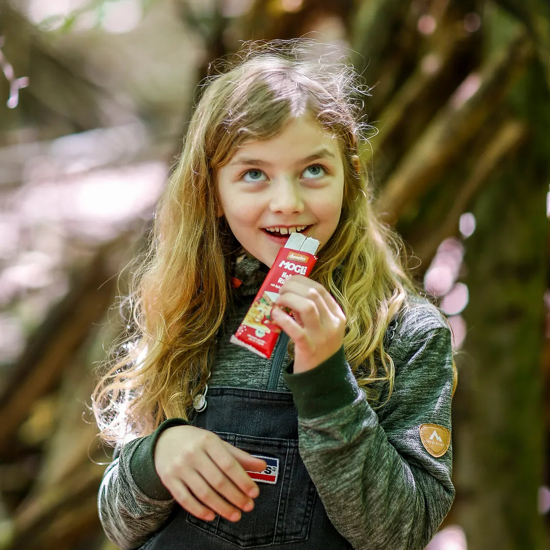 Mädchen steht im Wald und beißt in einen MOGLi Hafer Riegel.