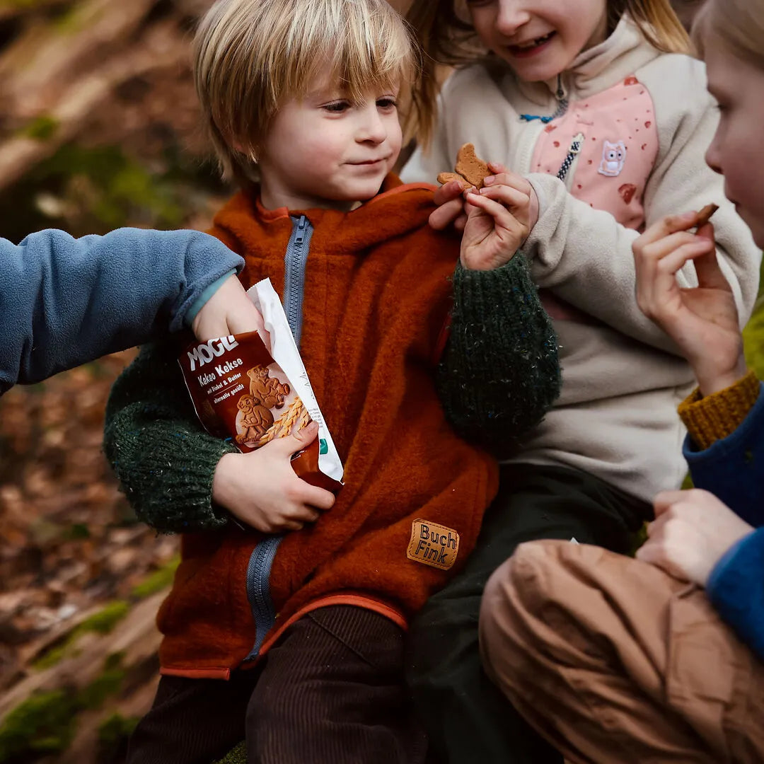 Kinder im Wald snacken MOGLi Kakao Kekse, eine Hand greift in die Packung und ein Junge hält die Packung in der Hand