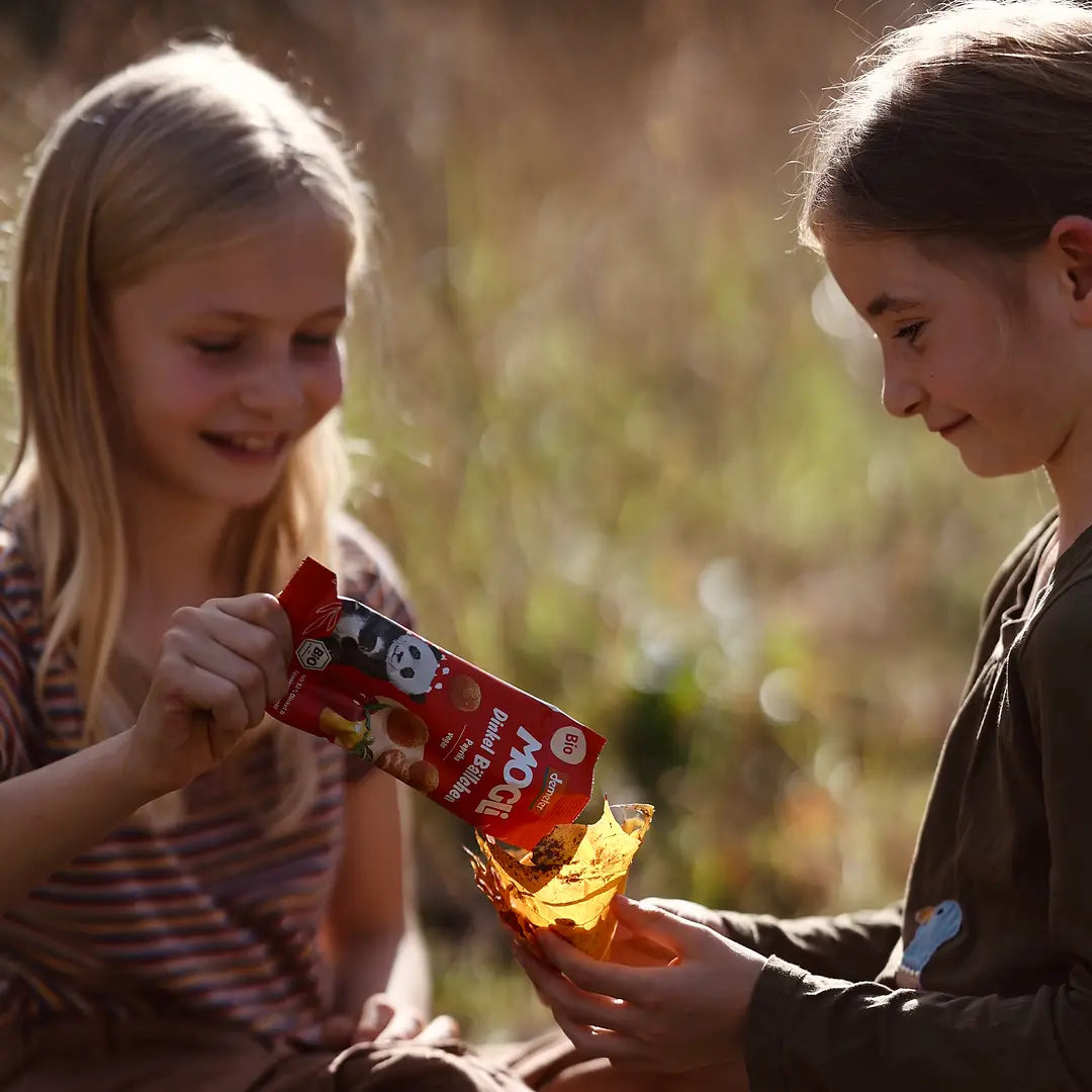 Ein Mädchen sitzt in der Natur und füllt eine Packung  MOGLi Dinkel Bällchen Paprika in eine Blätterschale.