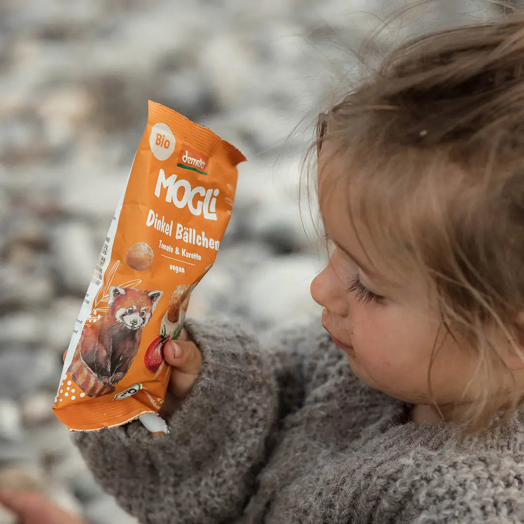 Kleines Mädchen hält eine Packung MOGLi Dinkel Bällchen Tomate in der Hand.