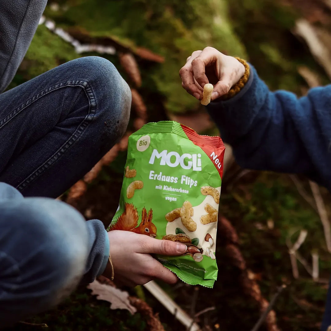 Kinderhand greift in die Packung MOGLi Erdnuss Flips, die Kinder sind im Wald.