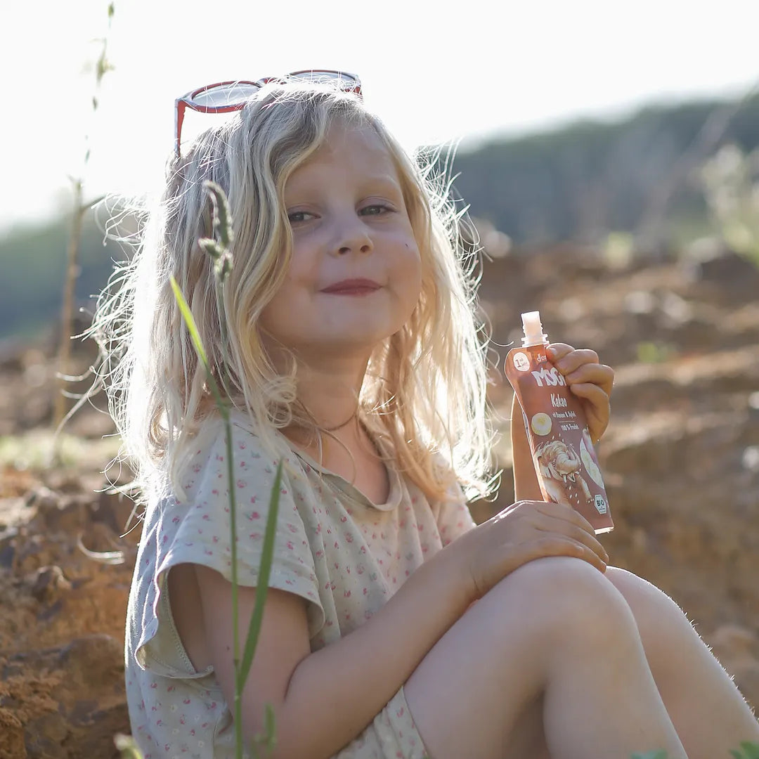 Mädchen sitzt in der Natur und trinkt einen MOGLi Kakao Quetschie.