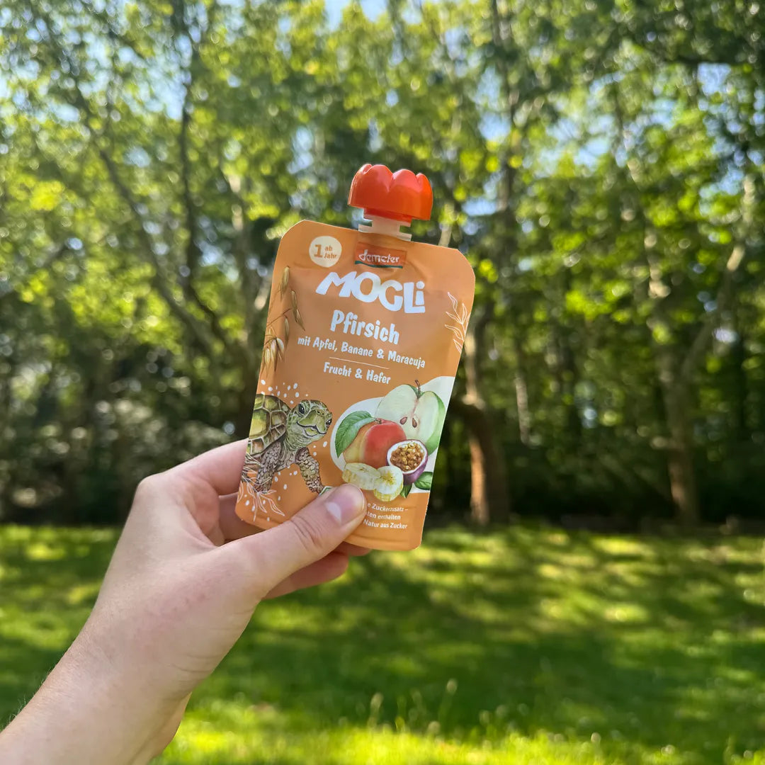 Eine Hand hält in einem Park einen MOGLi Pfirsich Quetschie in der Hand. 