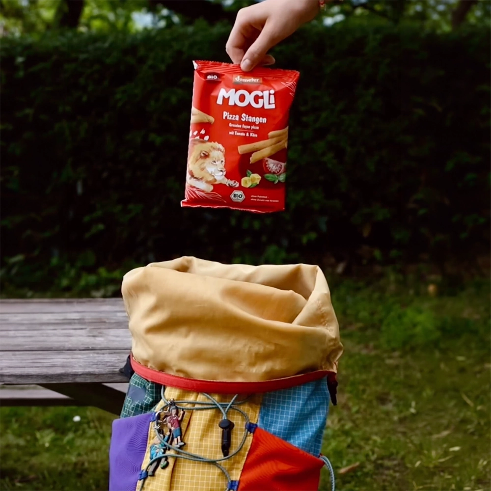 Eine ErwachseneHand packt den Rucksack mit MOGLi Pizza Stangen für den Familienausflug