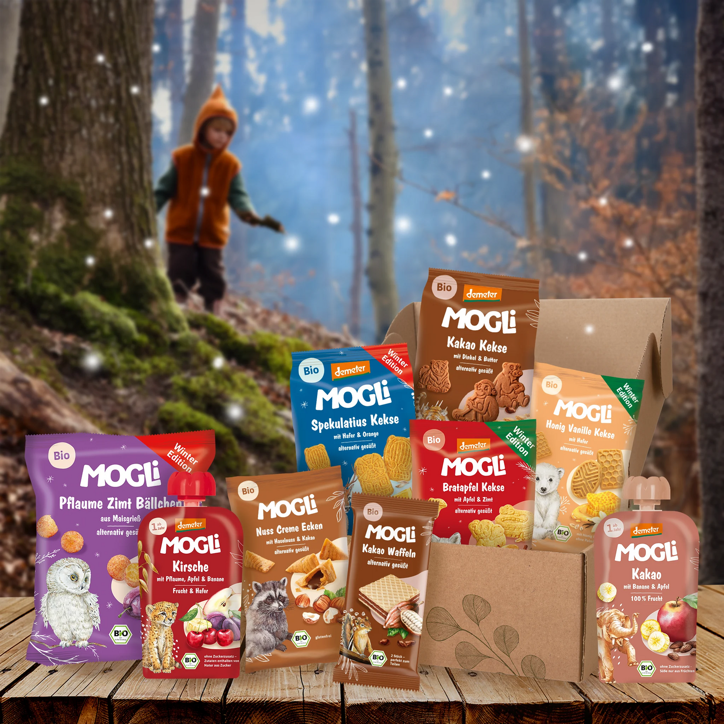 MOGLi Winter-Bundle mit Bio-Snacks für Kinder im winterlichen Wald: Kekse, Waffeln, Quetschies – natürlich lecker & weihnachtlich.
